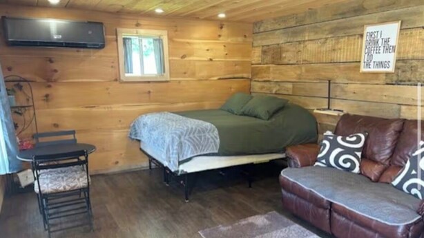 Ein gemütliches, blockhaussähnliches Zimmer mit einem Bett, einer Couch, einem Sessel, einem Fernseher und einem Fenster.