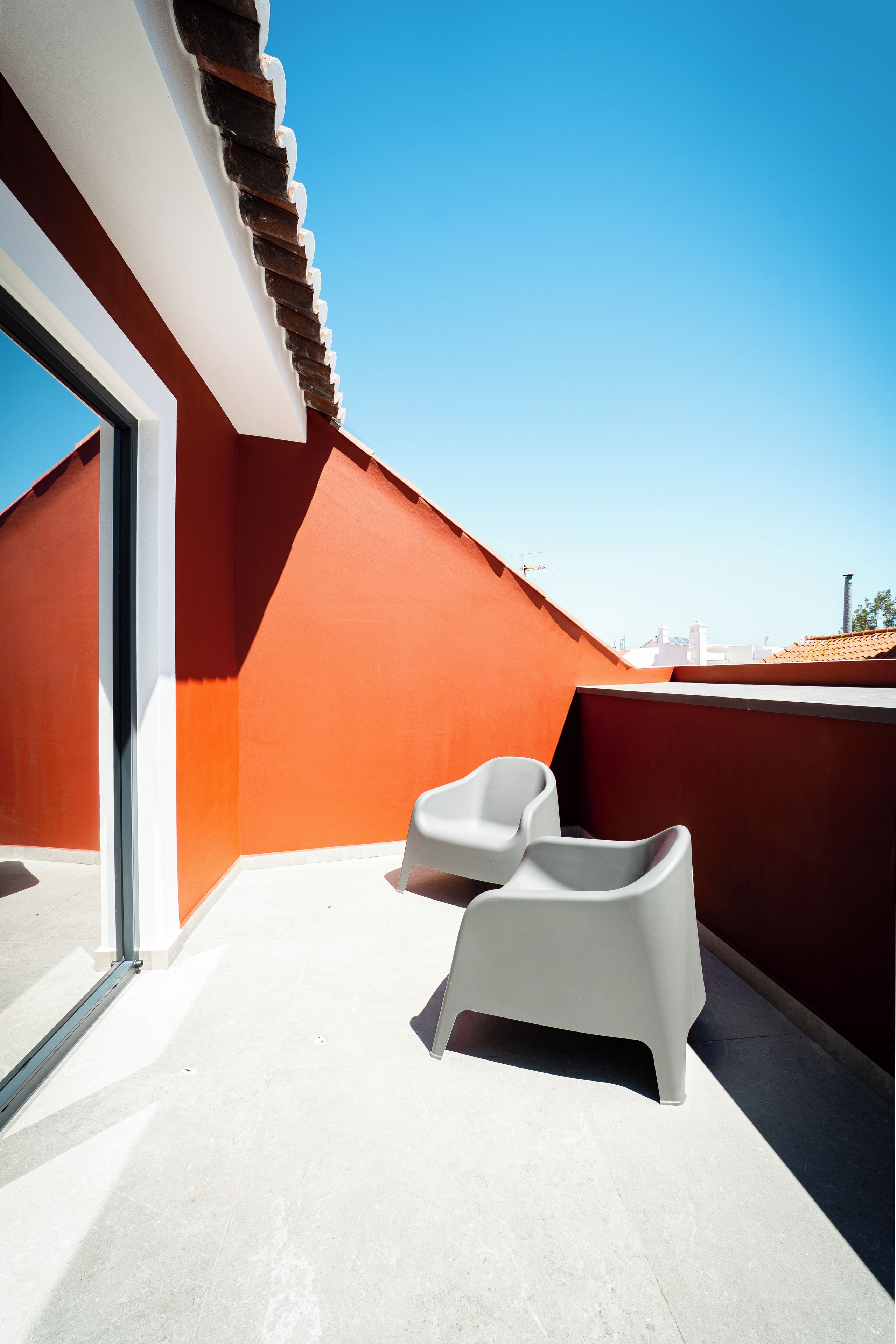 A rooftop terrace with a red wall, a white chair, and a clear blue sky.