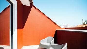 A rooftop terrace with a red wall, a white chair, and a clear blue sky.
