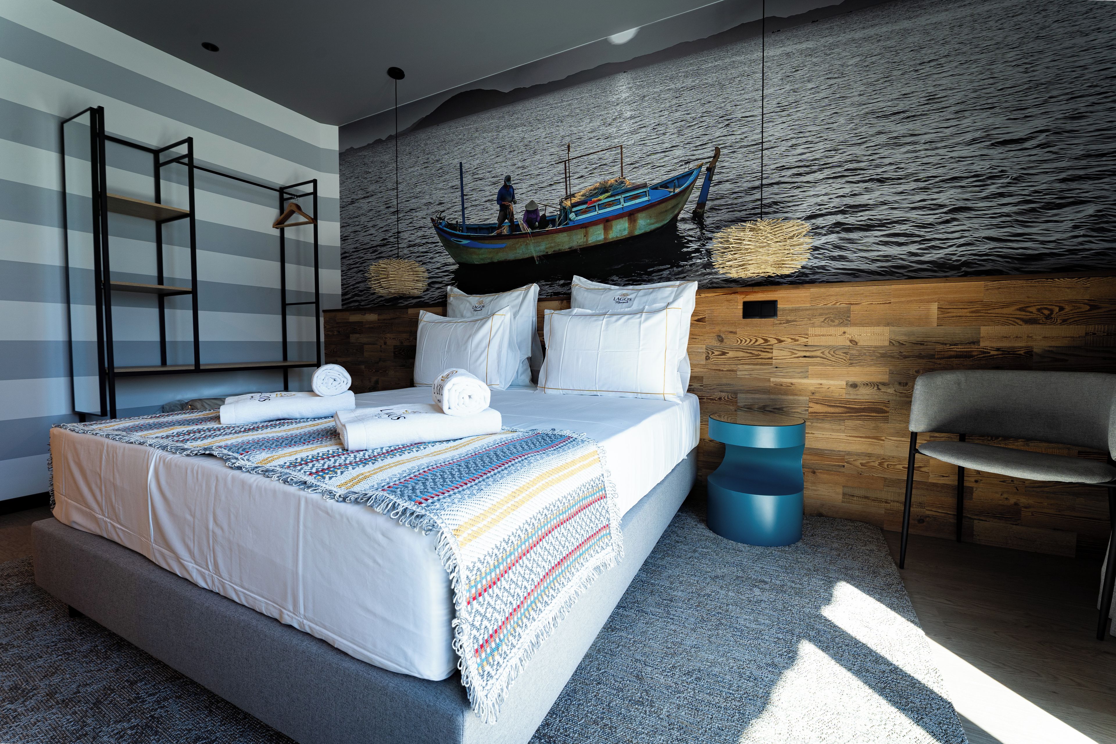 Een moderne slaapkamer met een groot bed, een houten hoofdbord, een decoratieve hangende boot en uitzicht op zee.