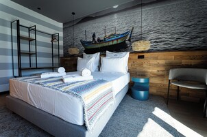 A modern bedroom with a large bed, a wooden headboard, a hanging boat decoration, and a view of the sea.