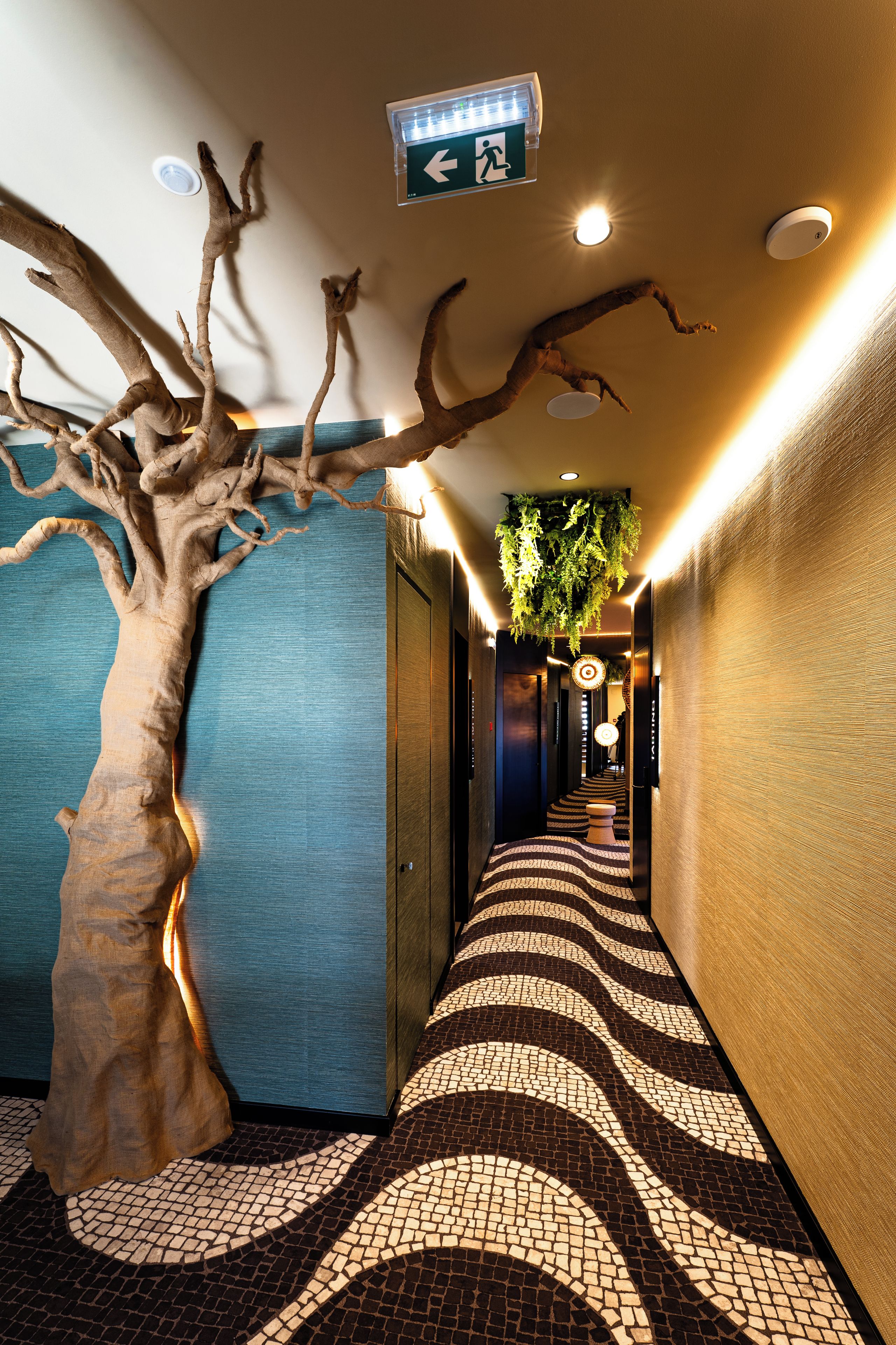 A hallway with a tree sculpture, patterned floor, and directional signage.