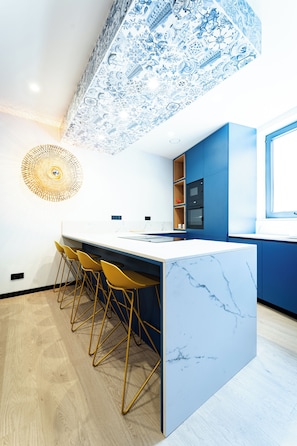 A modern kitchen with a marble island, bar stools, and blue cabinetry. - Lagos Moments Lodge (Lagos)