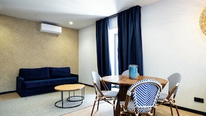 Ein modernes Wohnzimmer mit einer Couch, einem Esstisch mit Stühlen, einer Wand mit Muster und einem Fenster mit Vorhängen.