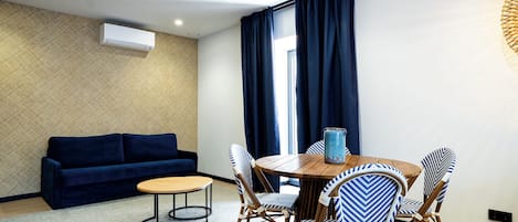 A modern living room with a sofa, a dining table with chairs, a patterned wall, and a window with curtains.