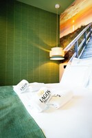 Habitación de hotel con cama, pared verde, un cuadro de un atardecer y una lámpara colgante.