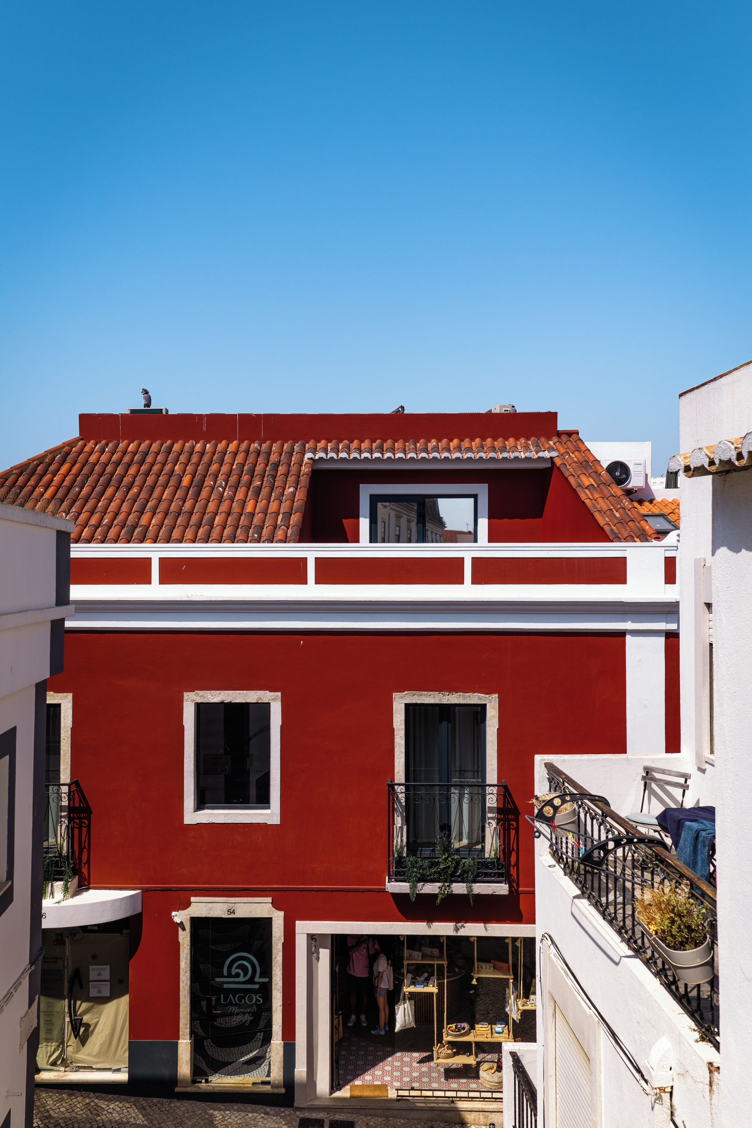 A red building with a tiled roof, a balcony with a metal railing, and a shop entrance.