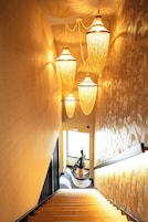 Una escalera con escalones de madera y barandilla negra, que conduce a una habitación con papel tapiz estampado y una estatua.