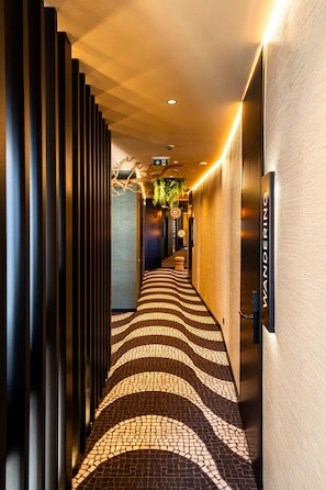 A hotel corridor with a patterned floor, vertical blinds, and a sign reading 'WANDERING'.