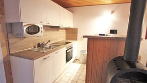 A compact kitchen with white cabinets, a microwave, a sink, an oven, and a wood-burning stove. - Schoner Doppelbungalow mit Terrasse im Ferienpark Mirow (Mirow)