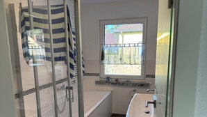 A modern bathroom with a glass shower enclosure, a bathtub, a sink, and a window providing natural light. - Quietly situated, yet right in the heart of it all. Fine sandy beach, horse farm / marina (Lubmin)