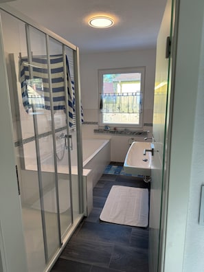 A modern bathroom with a glass shower enclosure, a bathtub, a sink, and a window providing natural light. - Quietly situated, yet right in the heart of it all. Fine sandy beach, horse farm / marina (Lubmin)