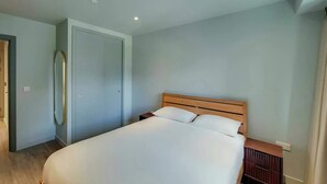 Un dormitorio con cama, cabecera de madera, mesita de noche y espejo en la pared.