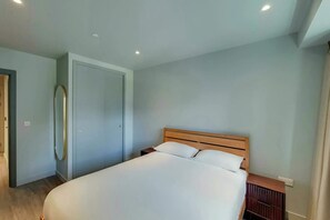 Un dormitorio con cama, cabecera de madera, mesita de noche y espejo en la pared.
