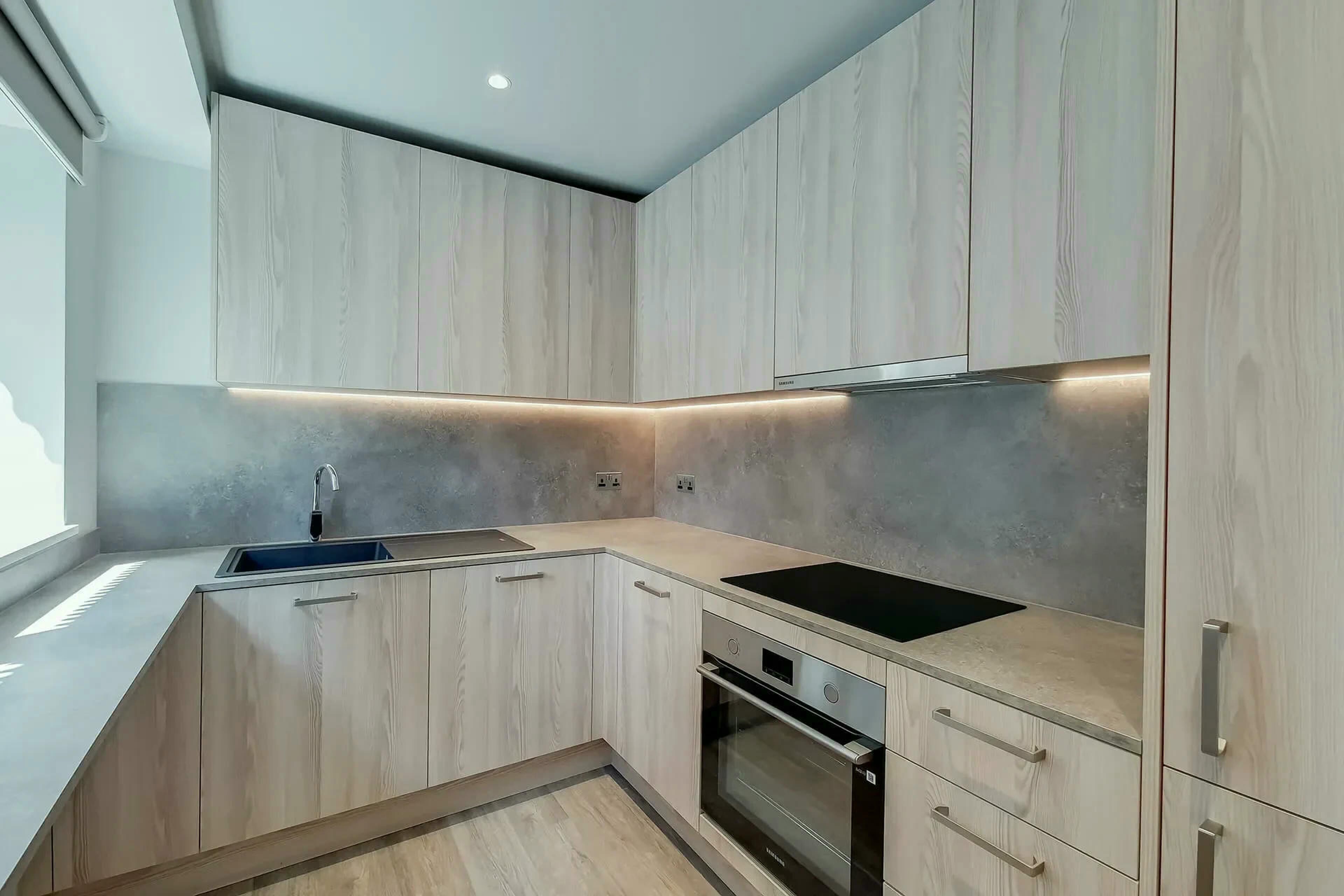 A modern kitchen with light wood cabinetry, a built-in oven, and a stainless steel sink.