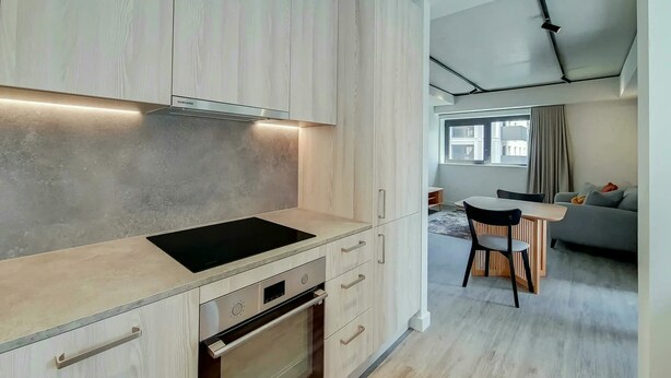 Una cocina moderna con horno integrado, un comedor con mesa y sillas, y una sala de estar con sofá y ventana.