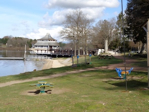 A lakeside park with picnic tables, a playground, and a building with a tower.