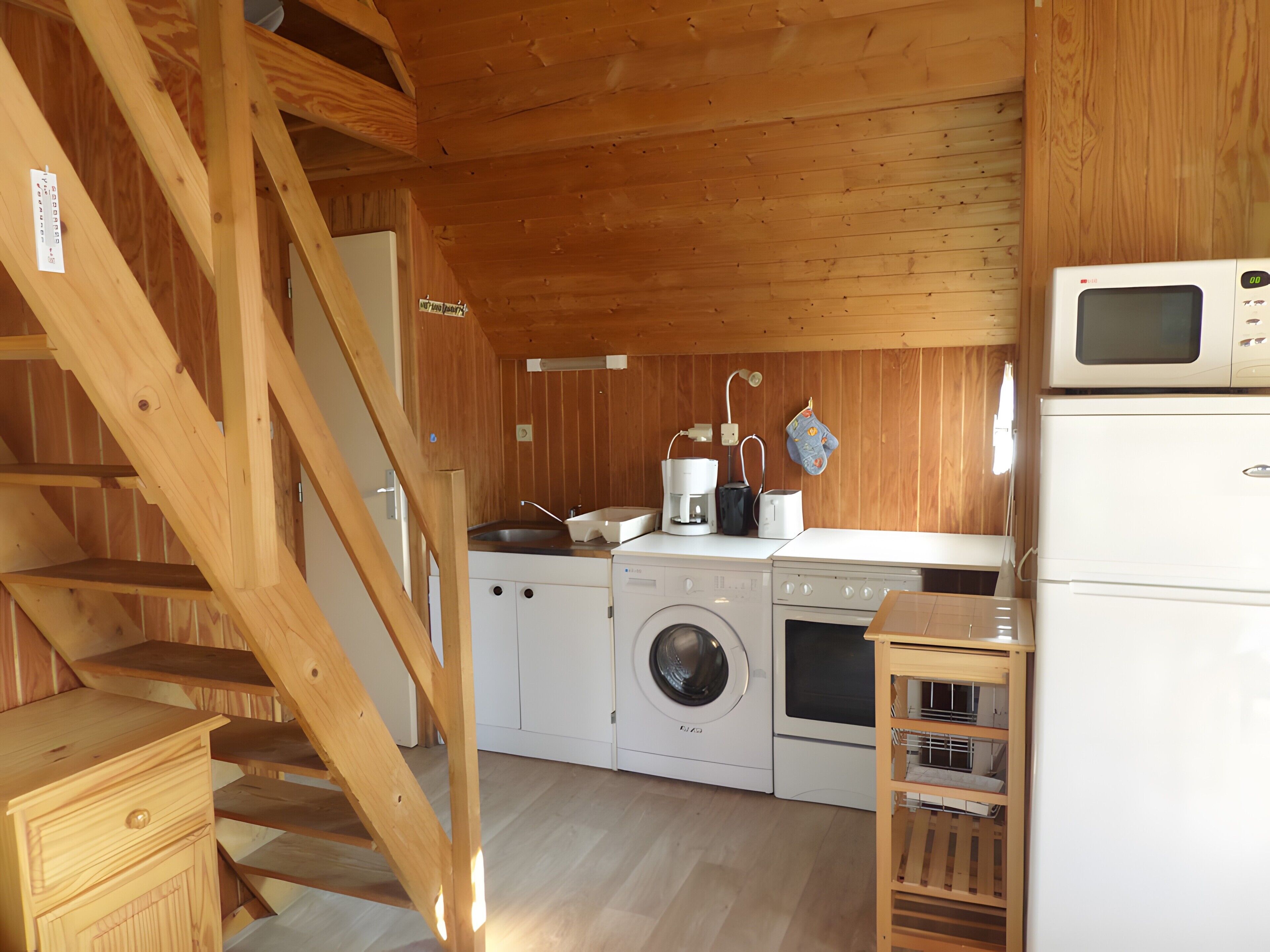 A compact kitchen with wooden beams, a washing machine, a microwave, and a coffee maker.