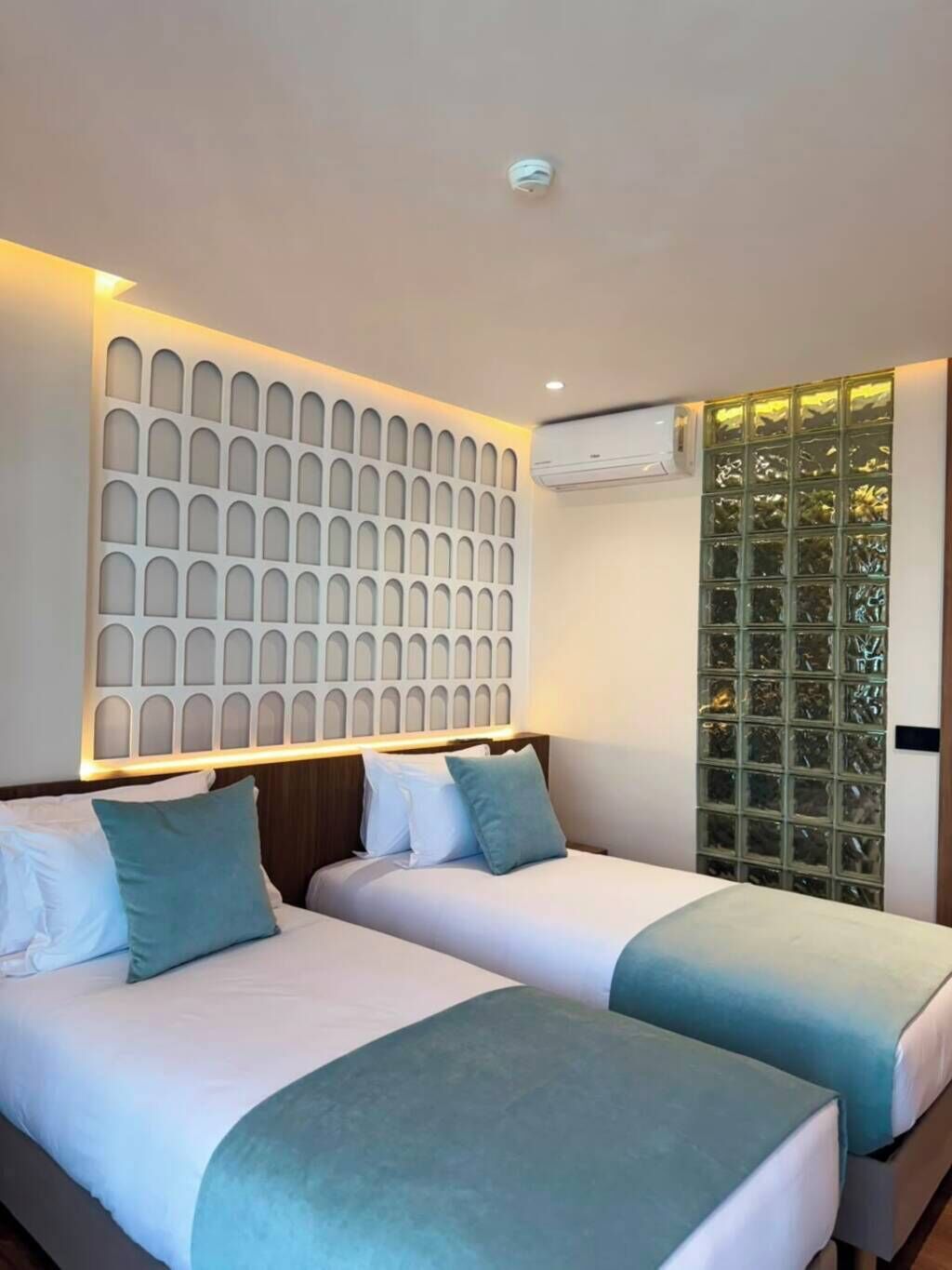 Une chambre d’hôtel avec deux lits, un panneau décoratif au mur, un appareil de climatisation et une fenêtre donnant sur un paysage agréable.