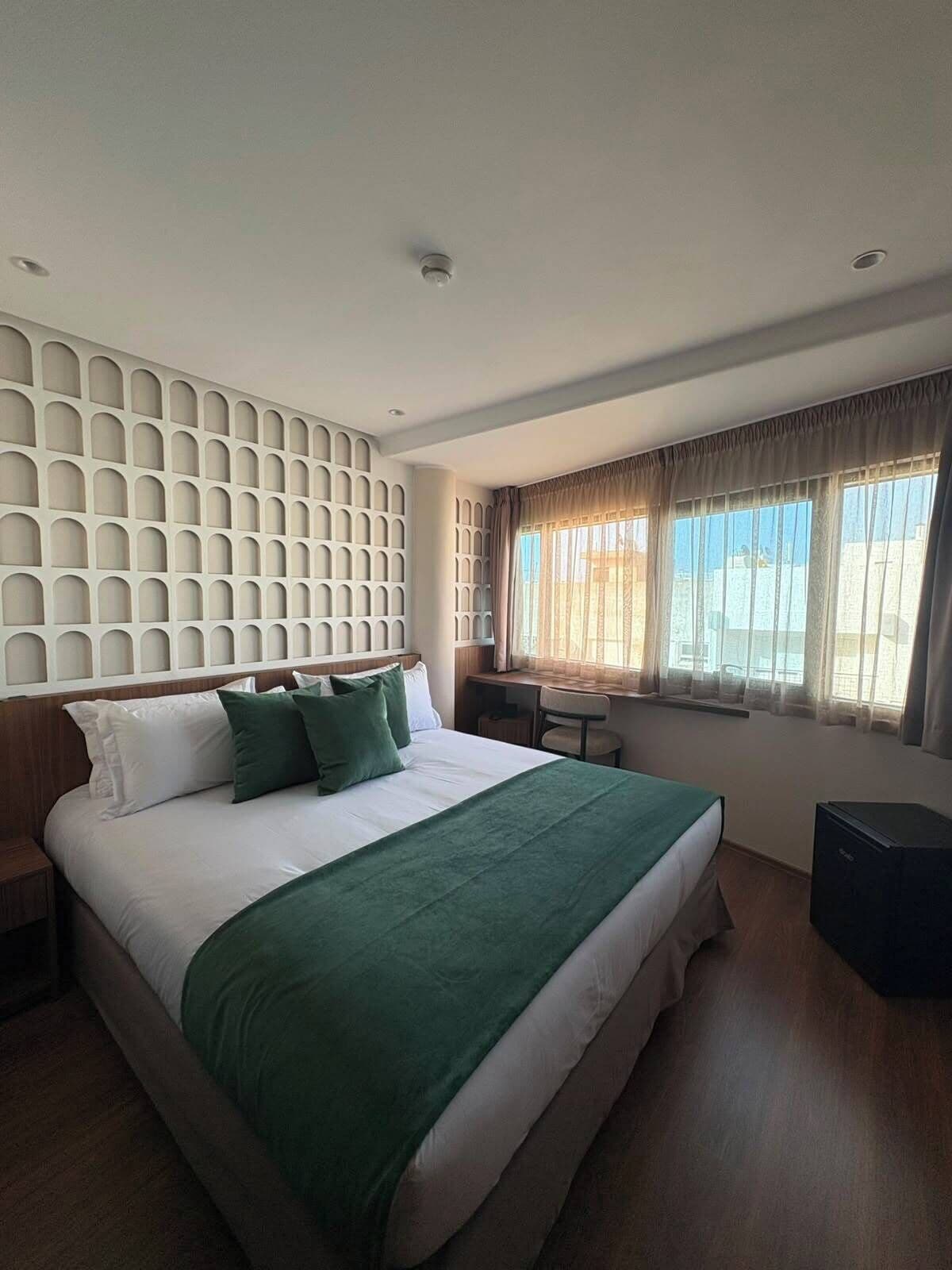 Ein Hotelzimmer mit einem großen Bett, einem Schreibtisch und einem Fenster mit Vorhängen.