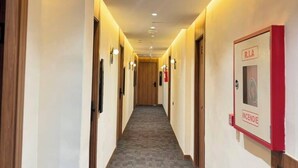 Un pasillo de hotel con puertas de madera, suelo alfombrado y un detector de incendios en la pared derecha.