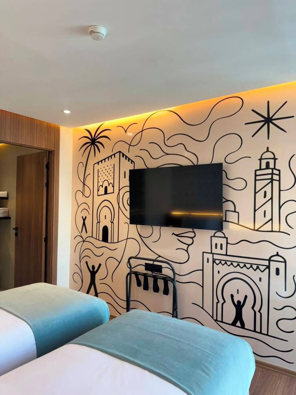 Une chambre d’hôtel comprenant un lit, un téléviseur à écran plat fixé au mur et une fresque décorative.