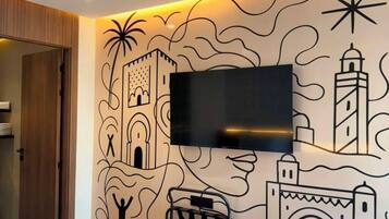 Une chambre d’hôtel comprenant un lit, un téléviseur à écran plat fixé au mur et une fresque décorative.