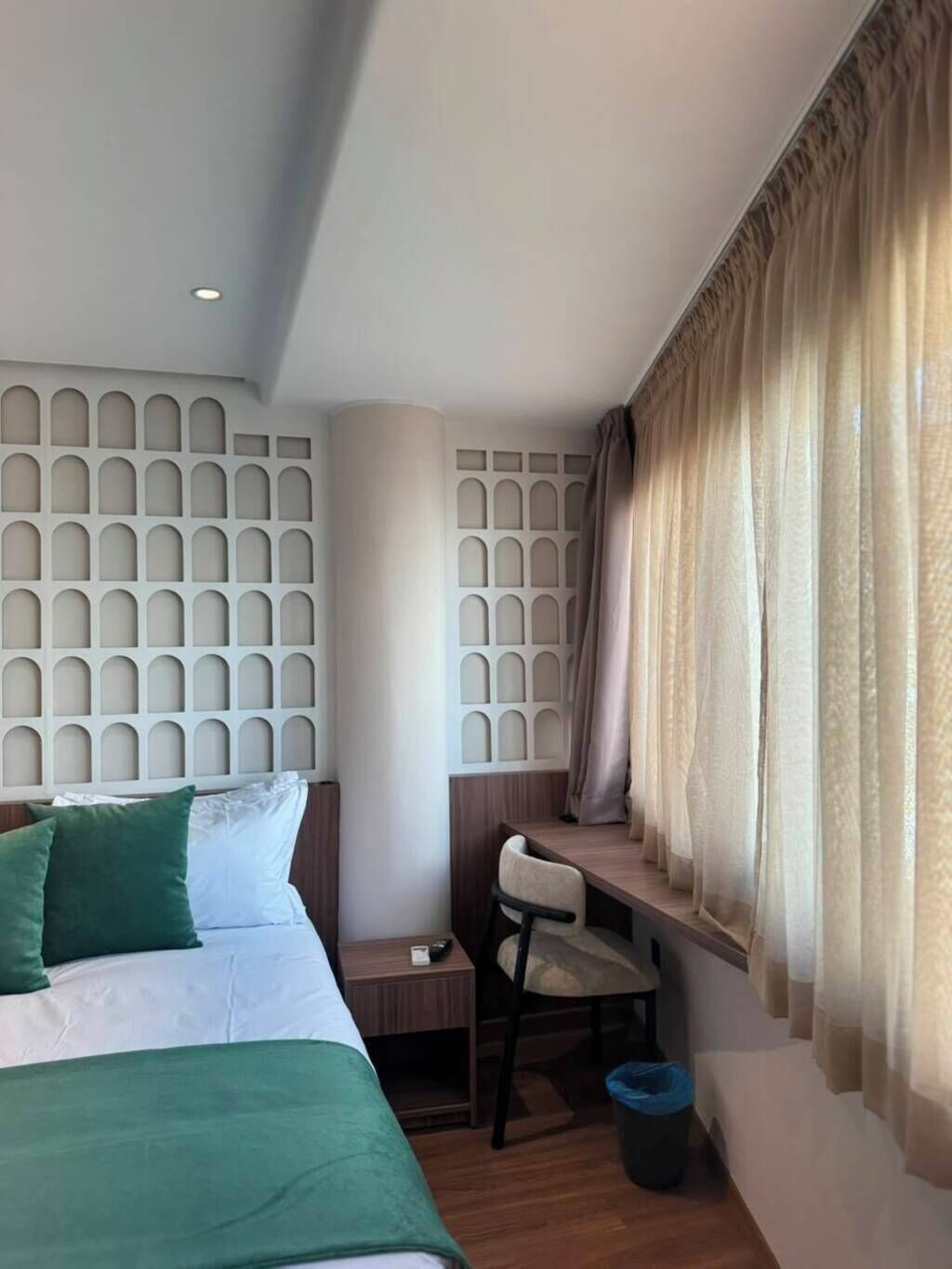 Una habitación de hotel con cama, escritorio, silla y ventana con cortinas.