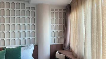 Una habitación de hotel con cama, escritorio, silla y ventana con cortinas.