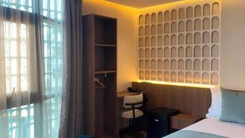 Une chambre d’hôtel comprenant un lit, un bureau, une chaise, une armoire et un mur orné d’un motif décoratif.