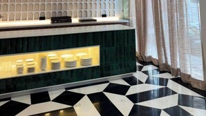 Un área de recepción moderna con piso estampado, un mostrador con exhibición iluminada y un gran ventanal con cortinas.