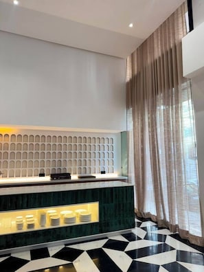 A modern reception area with a patterned floor, a counter with a lighted display, and a large window with curtains.