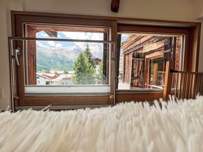 A room with a large window offering a view of a mountain landscape, wooden interior, and a fluffy white rug.