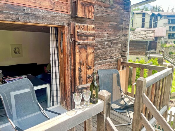 A rustic wooden outdoor seating area with a table, chairs, and a bottle of wine.