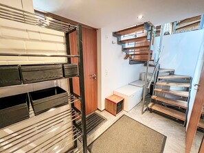 A compact, modern interior with a built-in bench, a small wooden cabinet, and a metal staircase.