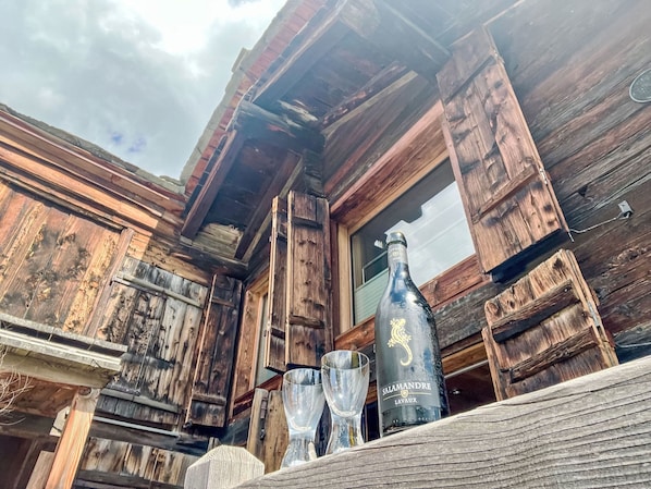 A rustic wooden cabin with a window and a bottle of wine on a table.