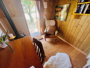 A wooden interior with a chair, a bookshelf, and a door leading outside. - Gorgeous shepherd’s hut: romantic, rustic, the perfect place to rest. (Henstridge)