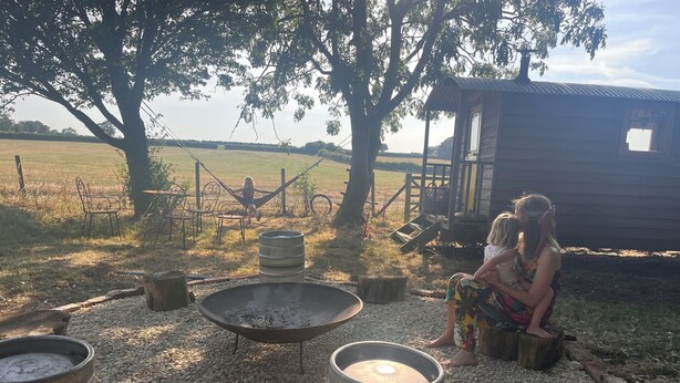 Un entorno rústico al aire libre con una estructura de madera, una fogata y una zona de estar.