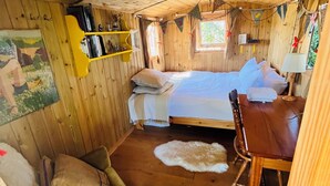 Acogedora habitación tipo cabaña de madera con cama, una silla, una mesa y una ventana.