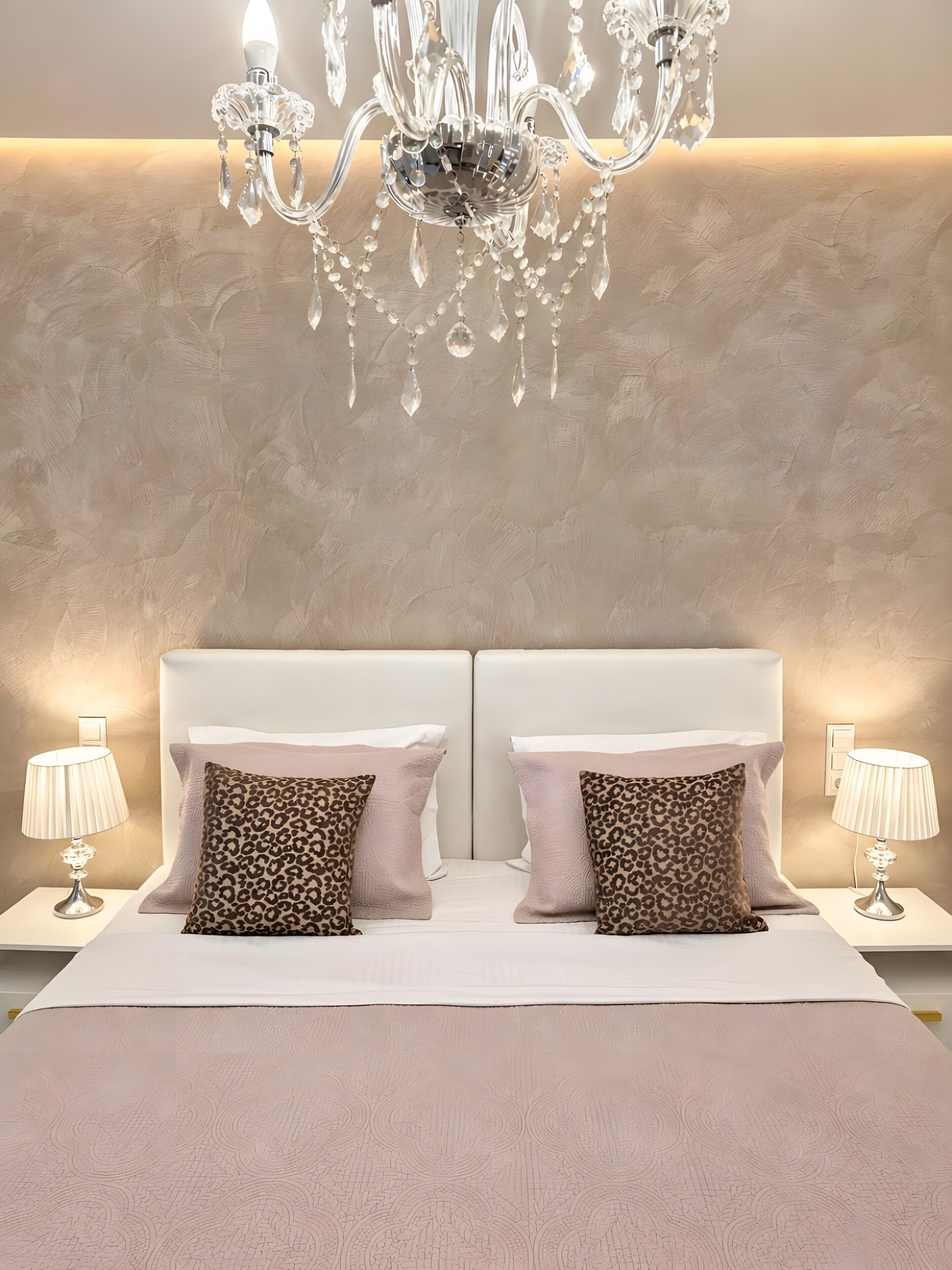 A bedroom with a chandelier, two nightstands, two lamps, and two leopard print pillows.