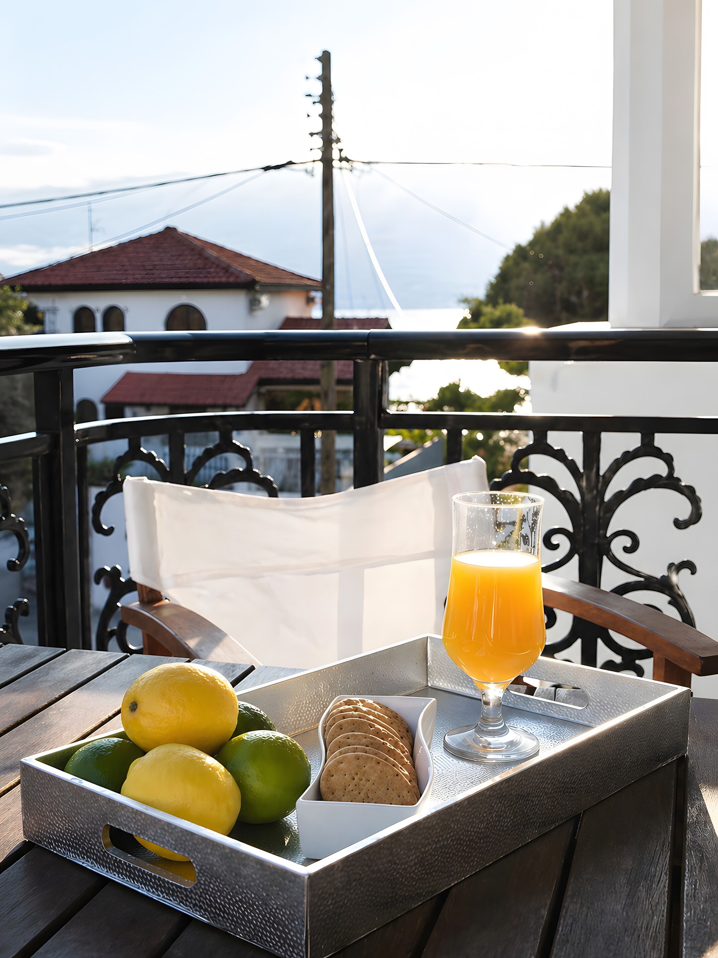 A tray with a glass of orange juice, a lemon, lime, and biscuits on a balcony with a view of buildings and a clear sky.