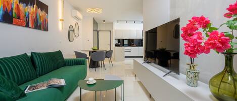A modern living room with a green sofa, a dining table, and a kitchen in the background.