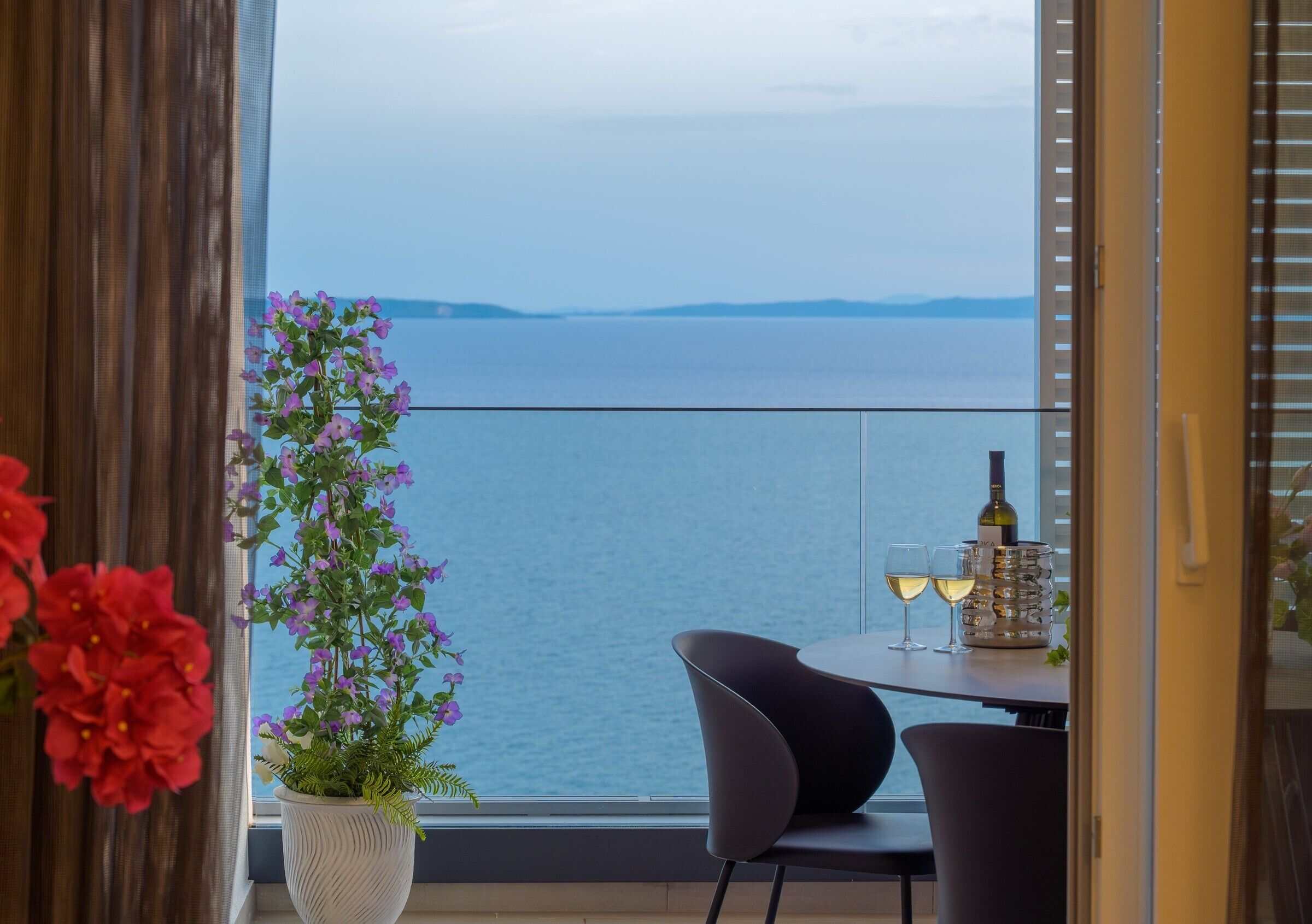 A balcony with a table, chairs, a bottle of wine, and a glass of wine.