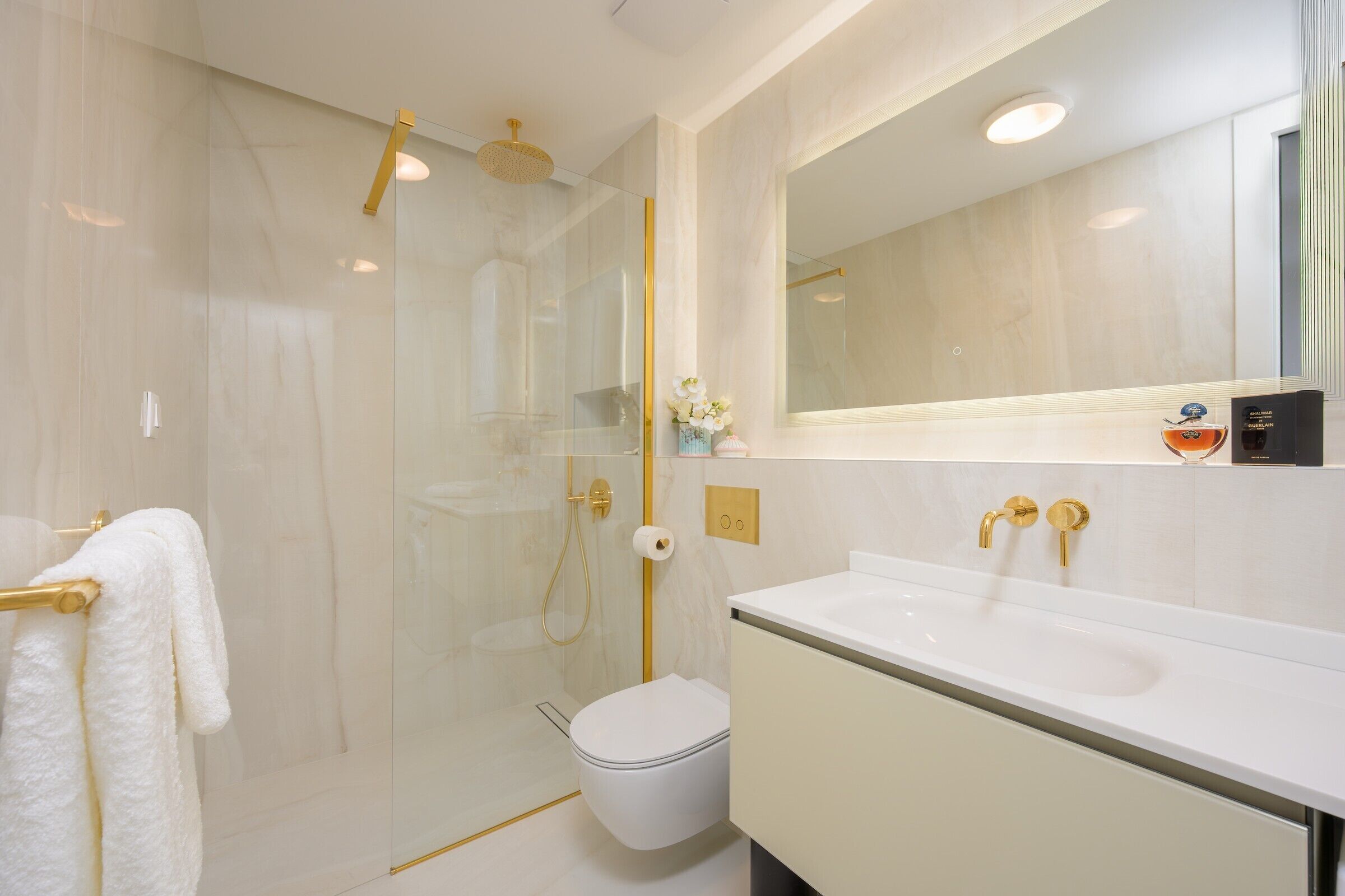 Ein modernes Badezimmer mit einer gläsernen Duschkabine, einer weißen Toilette und einem Waschtisch mit großem Spiegel.