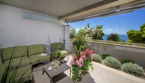A balcony with a green sofa, a small table with glasses and a cup, and a potted plant with pink flowers. - Apartment 'Green Eden' with Sea View, Wi-Fi and Air Conditioning (Split)