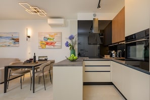 A modern kitchen with a dining area, featuring a central island, built-in appliances, and artwork on the walls. - Green Eden Apartment with Sea View, Wi-Fi, and Underfloor Heating (Split)