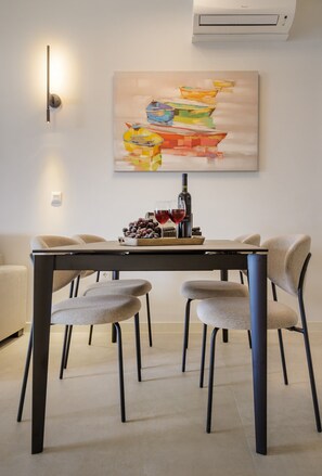A dining area with a table, chairs, a painting, and a bottle of wine. - Apartment 'Green Eden' with Sea View, Wi-Fi and Air Conditioning (Split)