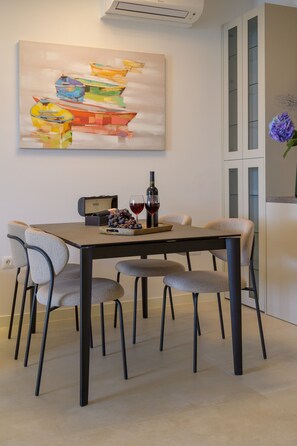 A dining area with a table set for four, a bottle of red wine, and a bowl of grapes. - Green Eden Apartment with Sea View, Wi-Fi, and Underfloor Heating (Split)