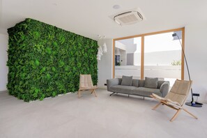 A modern living room with a green vertical garden wall, a grey sofa, two armchairs, and a large window. - Apartment 'Green Eden' with Sea View, Wi-Fi and Air Conditioning (Split)