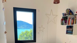 Une chambre avec une grande fenêtre, un lit, un bureau, un fauteuil poire et une bibliothèque.